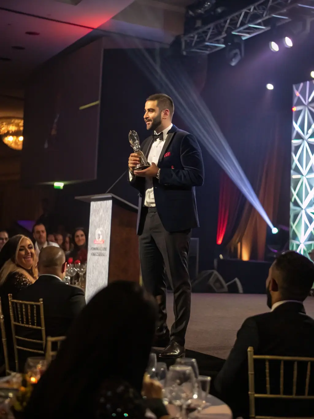 A successful Indian entrepreneur receiving an award on stage, with a cheering audience, highlighting the success stories resulting from the coaching services.
